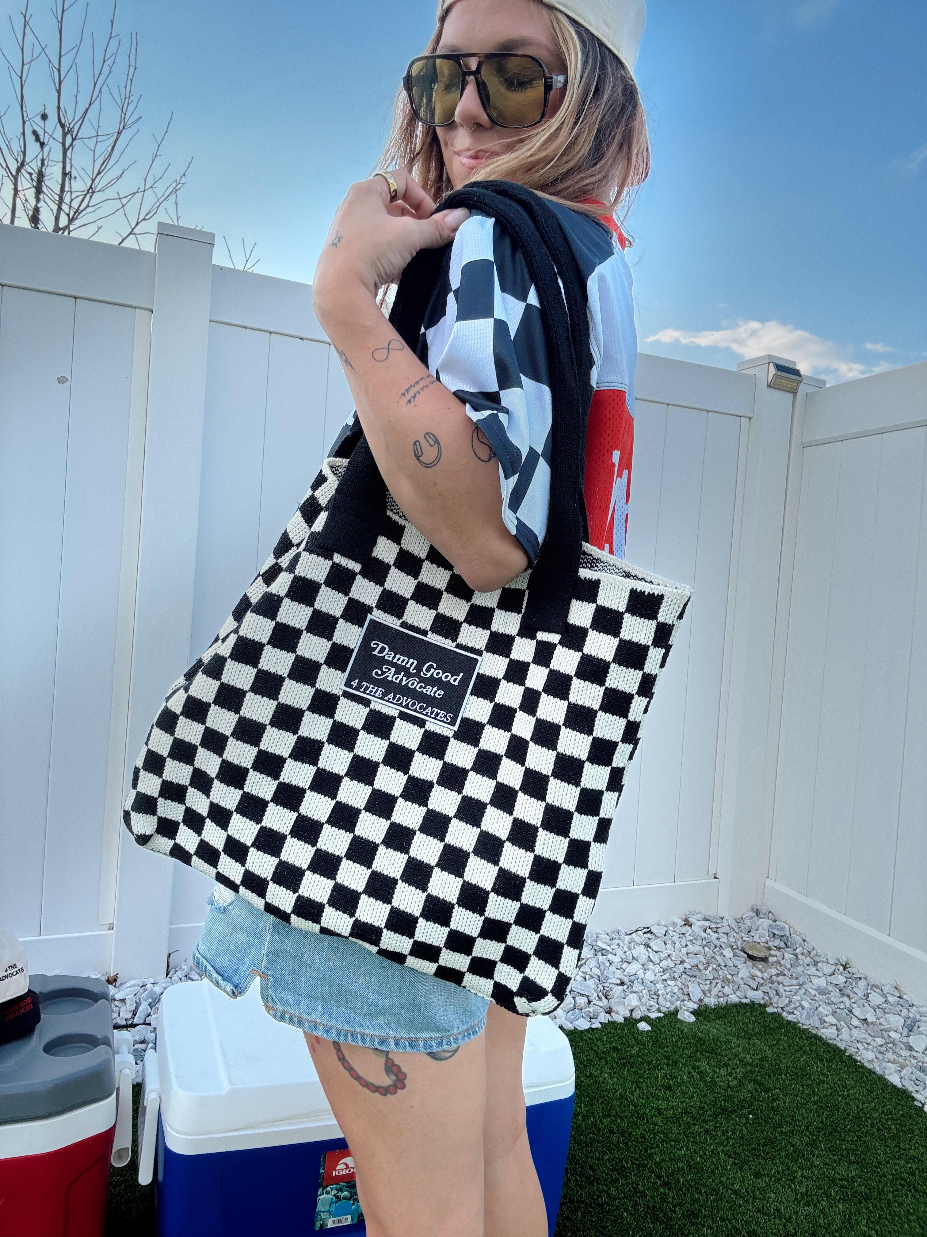 Person holding a checkered bag that says Damn Good Advocate outside. 