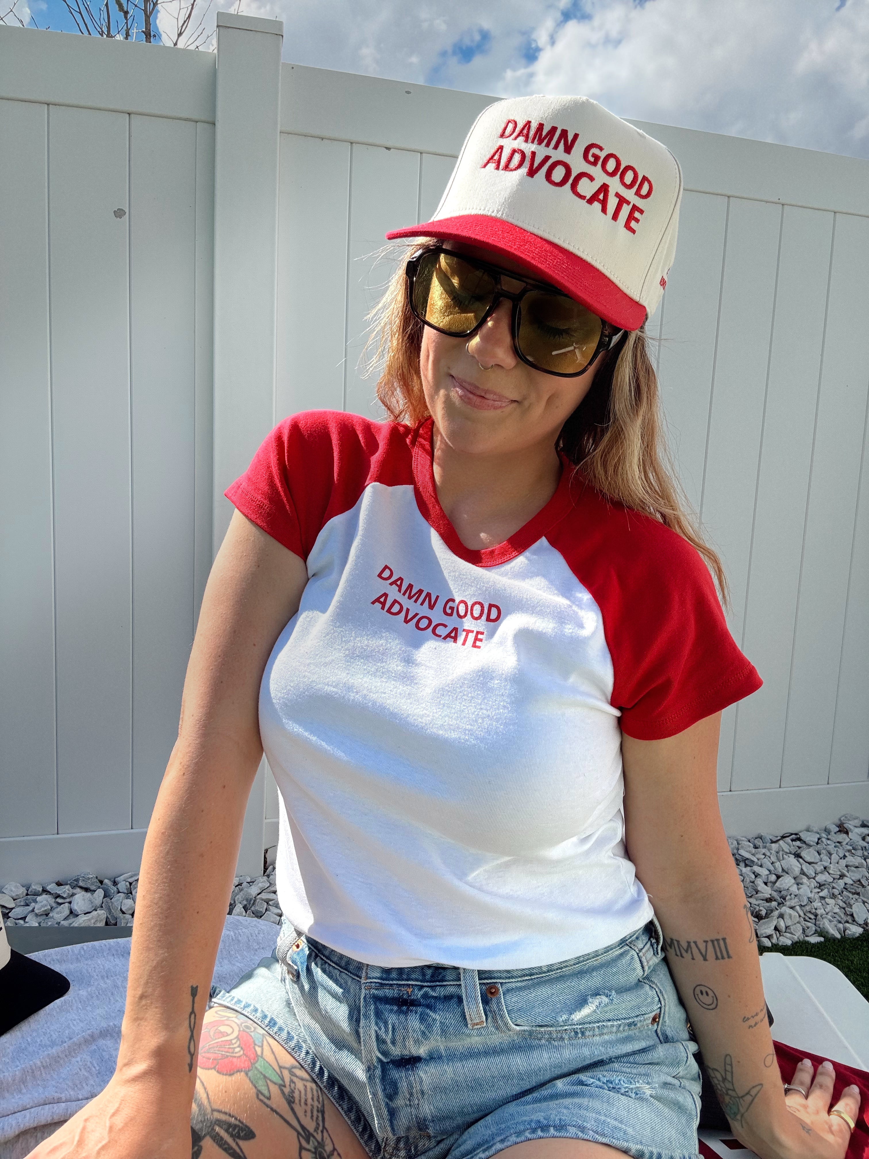Person wearing a 'Damn Good Advocate' t-shirt and cap outdoors.